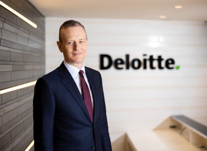Headshot of Deloitte Ireland CEO Harry Goddard with the Deloitte logo visible on a wall in the background.