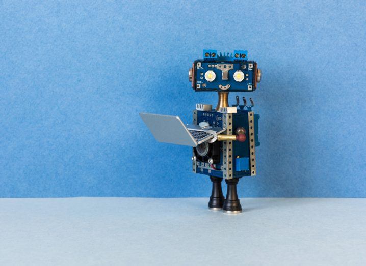 Tiny robot holding a laptop to represent AI in the workplace.