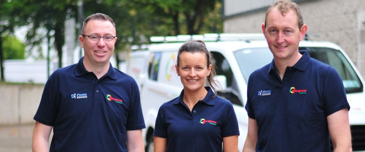 Two men stand on either side of a woman as they pose for a photo wearing t-shirts with the Energywise Ireland logo on them.