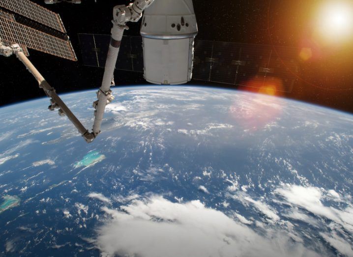 The Earth being viewed from an orbit, with parts of a space station visible and the sun in the distance.