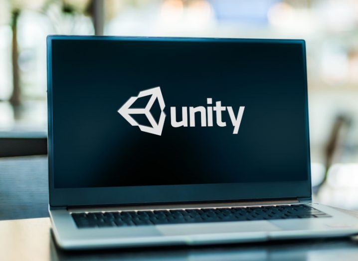 The Unity logo on a laptop screen, which sits on a table in an office environment.