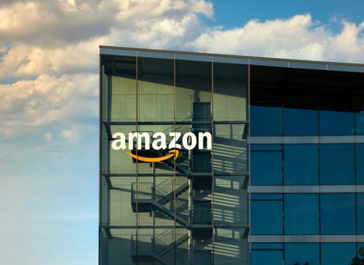 The Amazon logo on the side of a tall building, with a blue sky and clouds behind it.