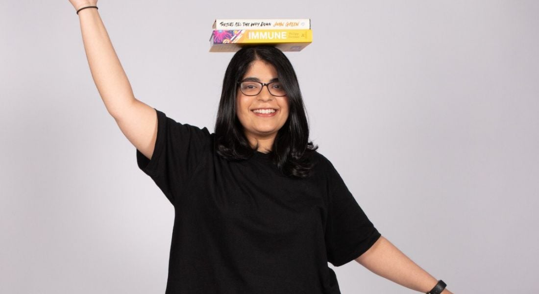 A woman stands with her arms outstretched while balancing two books on her head. She is Arushi Doshi, a manager working in cybersecurity and forensics at Deloitte.