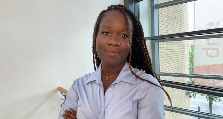 A woman wearing a light blue shirt smiles with her arms crossed in an office setting. She is Blessing Folayan, a radiographer and technology consulting analyst at Deloitte.
