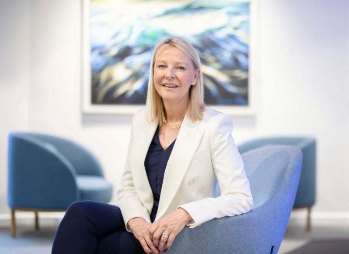 A woman sitting on a blue chair in a room with more chairs and a painting in the background. She is Catherine Doyle of Dell Technologies Ireland.