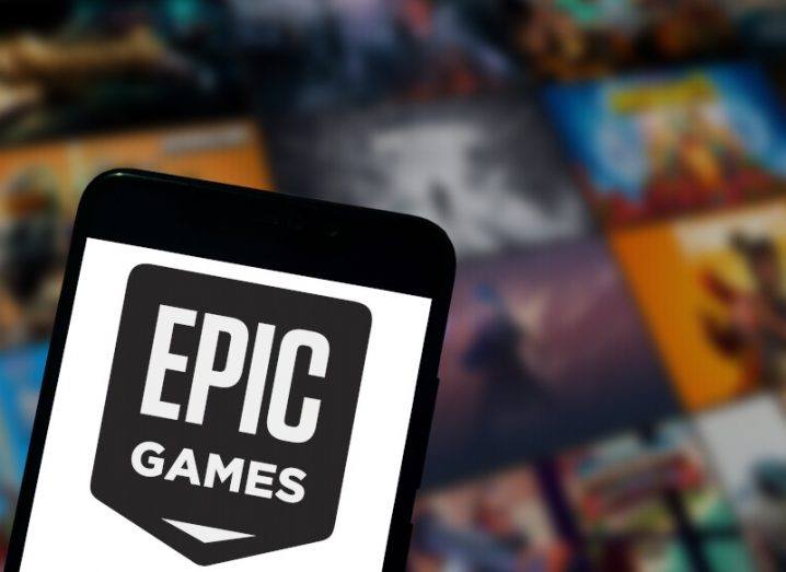 An Epic Games logo on a phone screen is large in the foreground with Epic Games images blurred in the background.