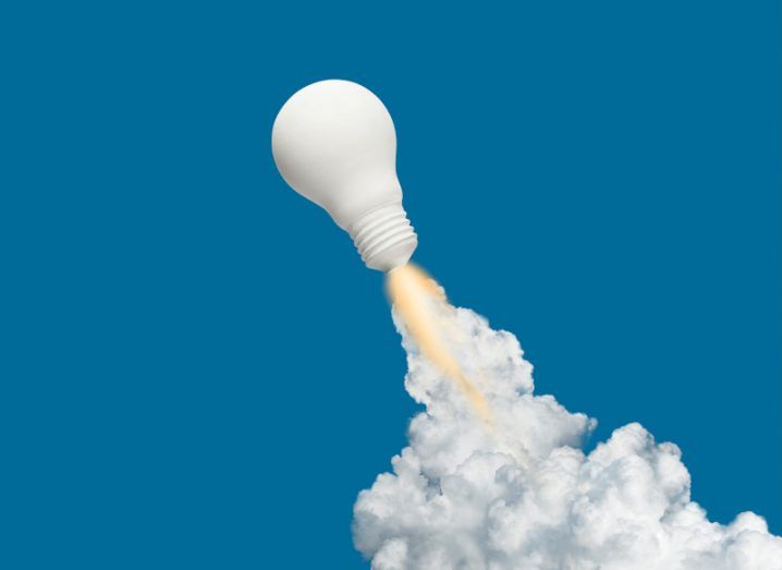 A lightbulb is positioned like a rocket blasting off, with flames and smoke coming from the bottom of it.