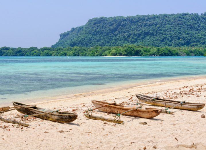 Small boats on a white sandy beach with a turquoise blue ocean and greenery behind it.