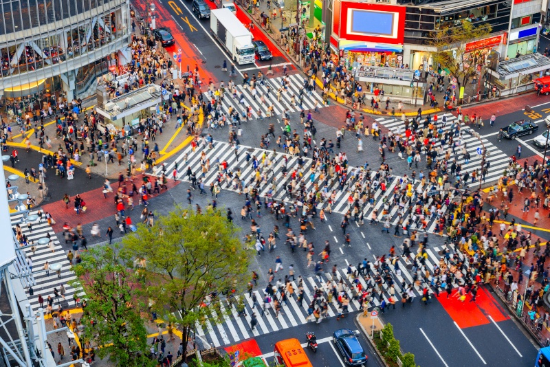 Several zebra crossings in Shibuya, Tokyo with many people and large buildings around the roads.