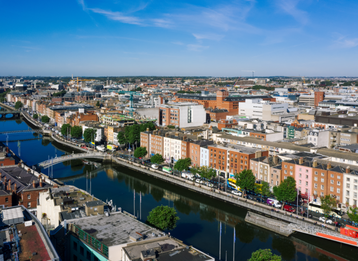 An aerial view of the Liffey river in Dublin, under a blue sky with buildings surrounding it.
