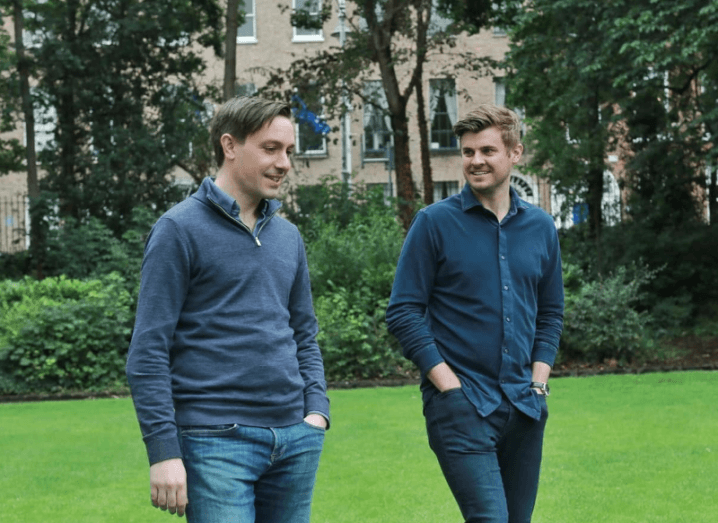 Wayflyer founders Aidan Corbett and Jack Pierse walking and having a conversation in a green field with trees in the background.